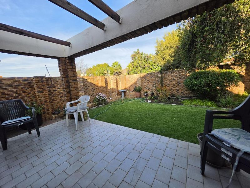 A covered patio area featuring tiled flooring, brick support columns, and a pergola, overlooking a private garden with brick boundary walls.