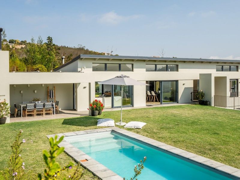 A modern rear exterior view featuring a swimming pool, a covered patio area with an outdoor fireplace, and large sliding glass doors.