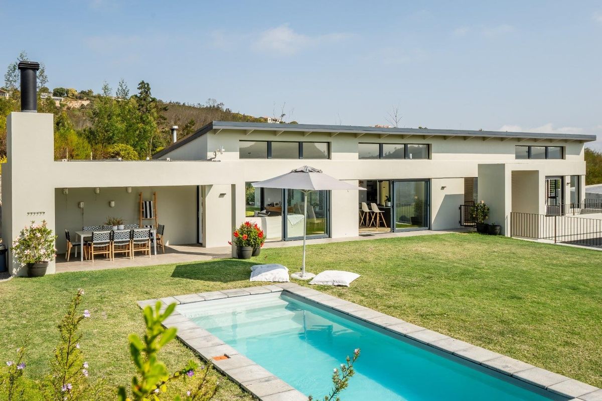 A modern rear exterior view featuring a swimming pool, a covered patio area with an outdoor fireplace, and large sliding glass doors.
