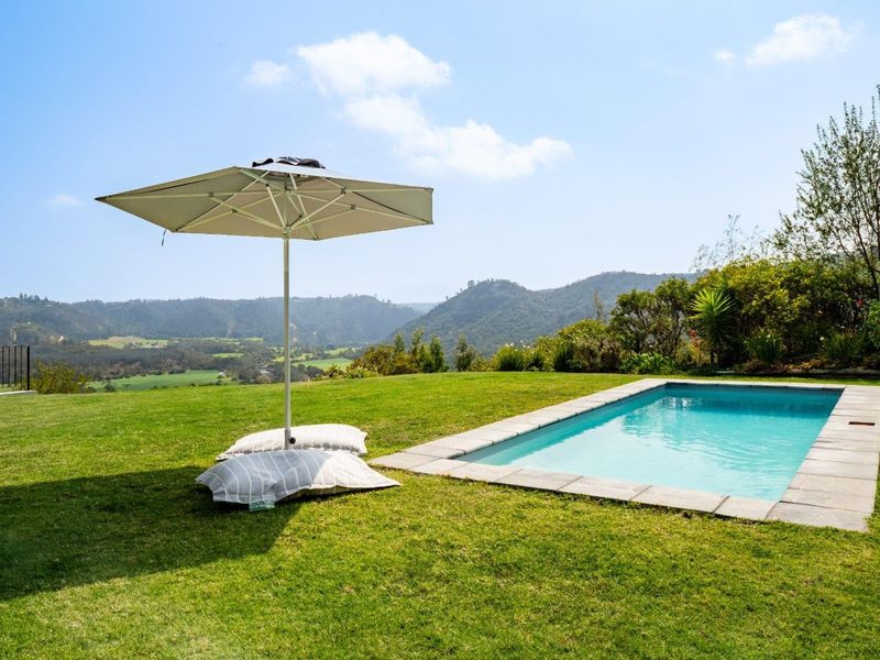A well-maintained swimming pool set within a lush green lawn, featuring stone coping and expansive mountain views.
