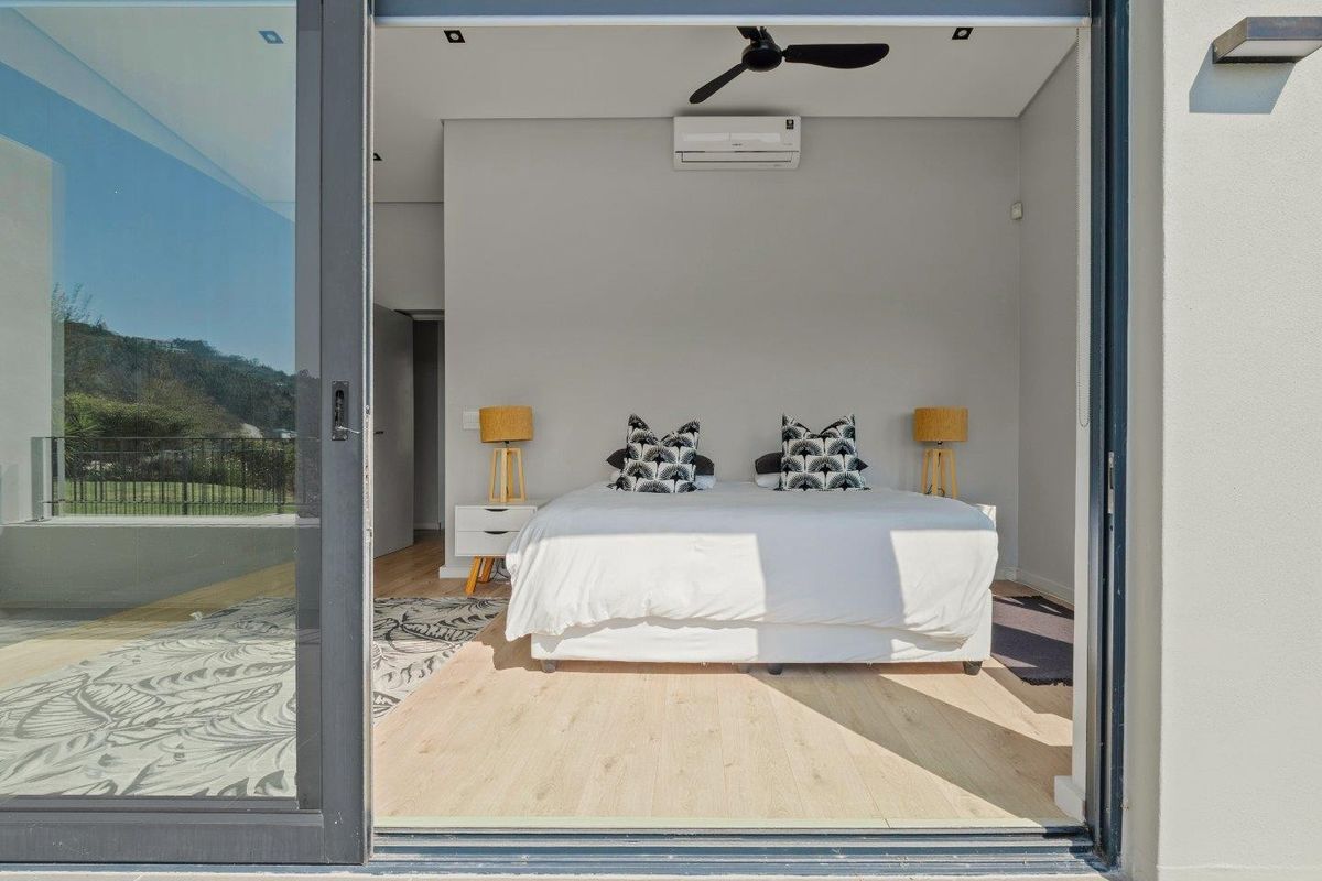 Modern bedroom featuring light laminate flooring, a ceiling fan, and a split-system air conditioner, with large sliding glass doors opening to an outdoor area.