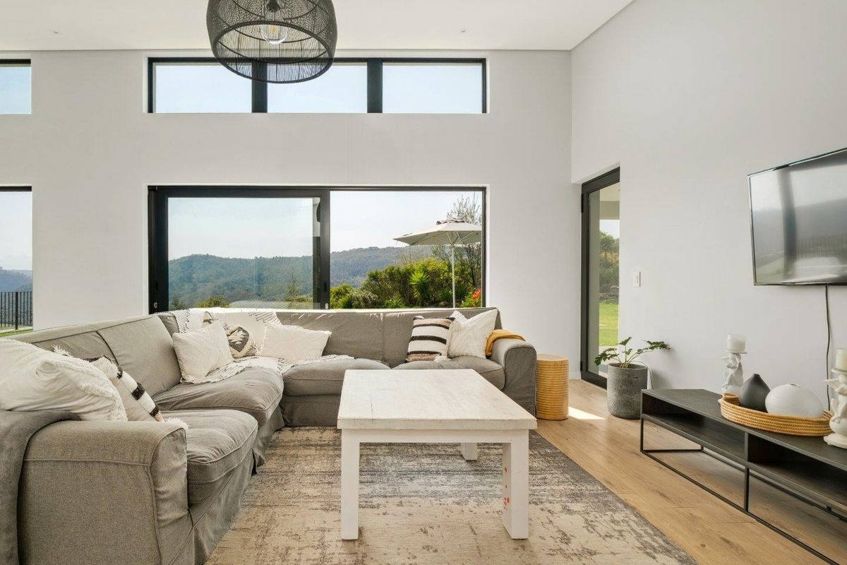Spacious, modern living room featuring high ceilings, large sliding glass doors with scenic views, and light timber flooring.