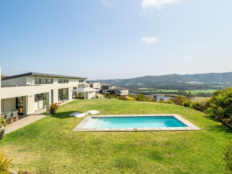 A well-maintained rear garden featuring a swimming pool with stone coping, a covered patio area, and expansive views of the surrounding landscape.