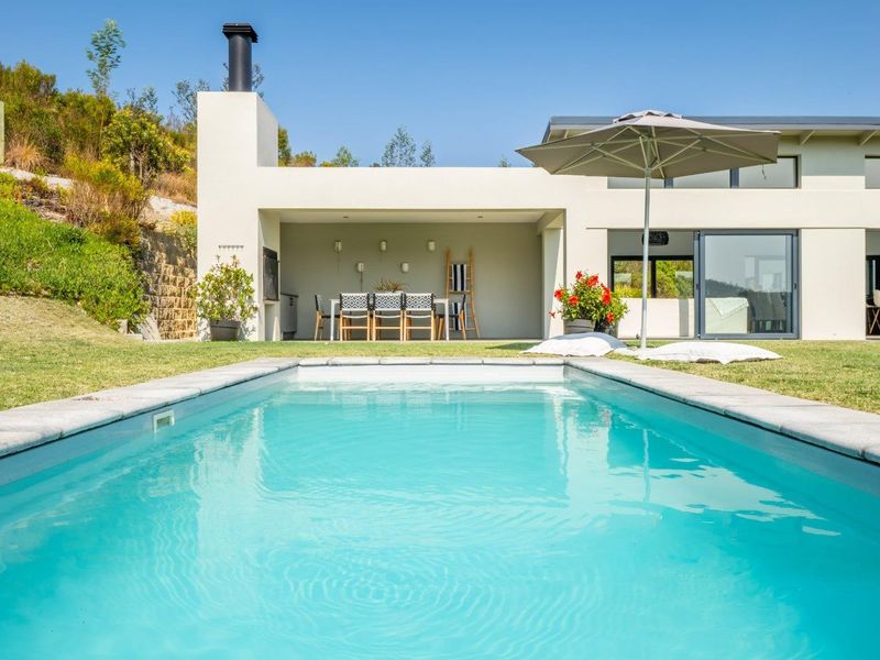 A well-maintained swimming pool area featuring a covered patio with a built-in braai, overlooking a landscaped garden and modern home exterior.