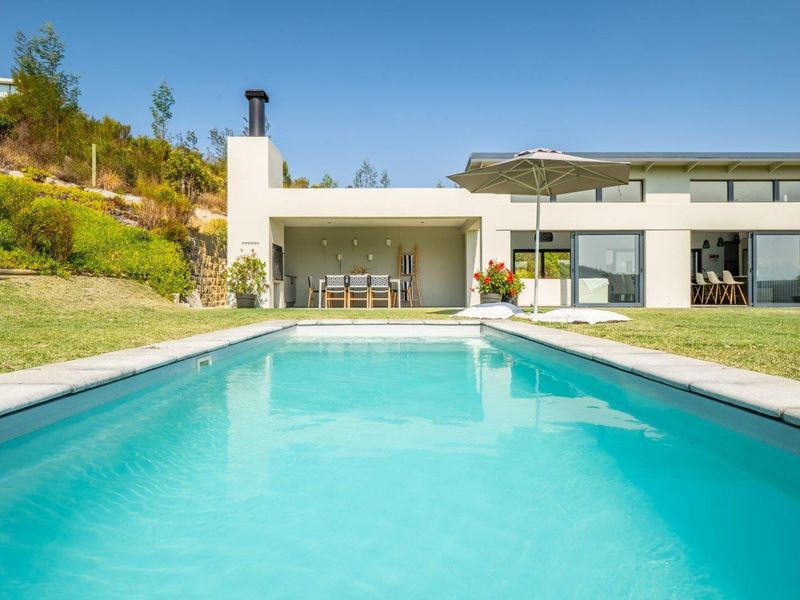 A well-maintained swimming pool with stone coping, adjacent to a modern covered patio featuring a built-in fireplace and large sliding glass doors.