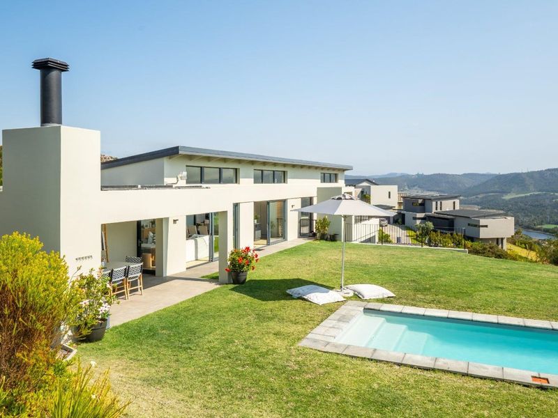 Rear exterior view featuring a modern home with a covered patio, swimming pool, and expansive lawn overlooking scenic hills.