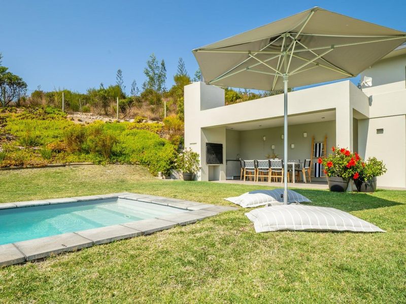 A well-maintained outdoor area featuring a swimming pool with stone coping, a covered patio with a built-in braai, and a landscaped garden.