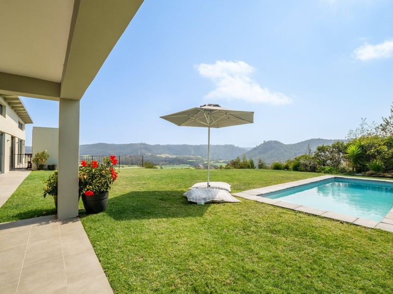 A well-maintained outdoor pool area featuring a tiled patio, lush lawn, and scenic mountain views.