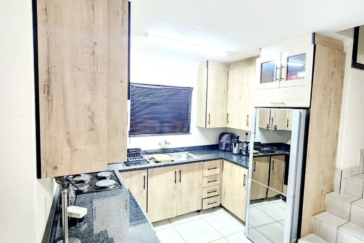 Modern kitchen featuring light wood-look cabinetry, dark granite countertops, tiled flooring, and an integrated staircase leading to the upper level.