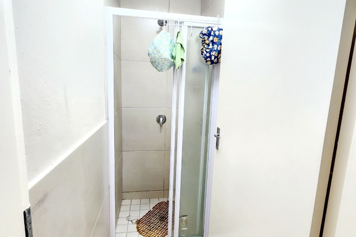 A compact bathroom featuring a tiled shower enclosure with a glass door and neutral wall tiling.