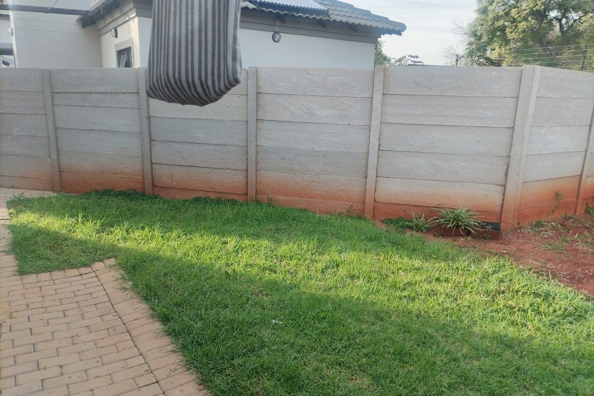 A rear garden area featuring a lawn, paved walkway, and a precast concrete boundary wall with visible weathering.