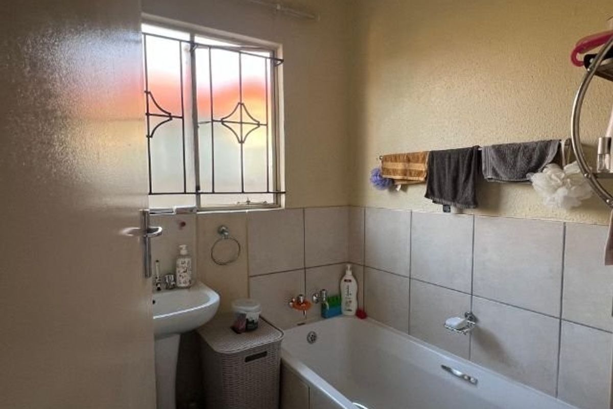 A functional bathroom featuring a pedestal basin, bathtub with tiled splashback, and a window with security bars.