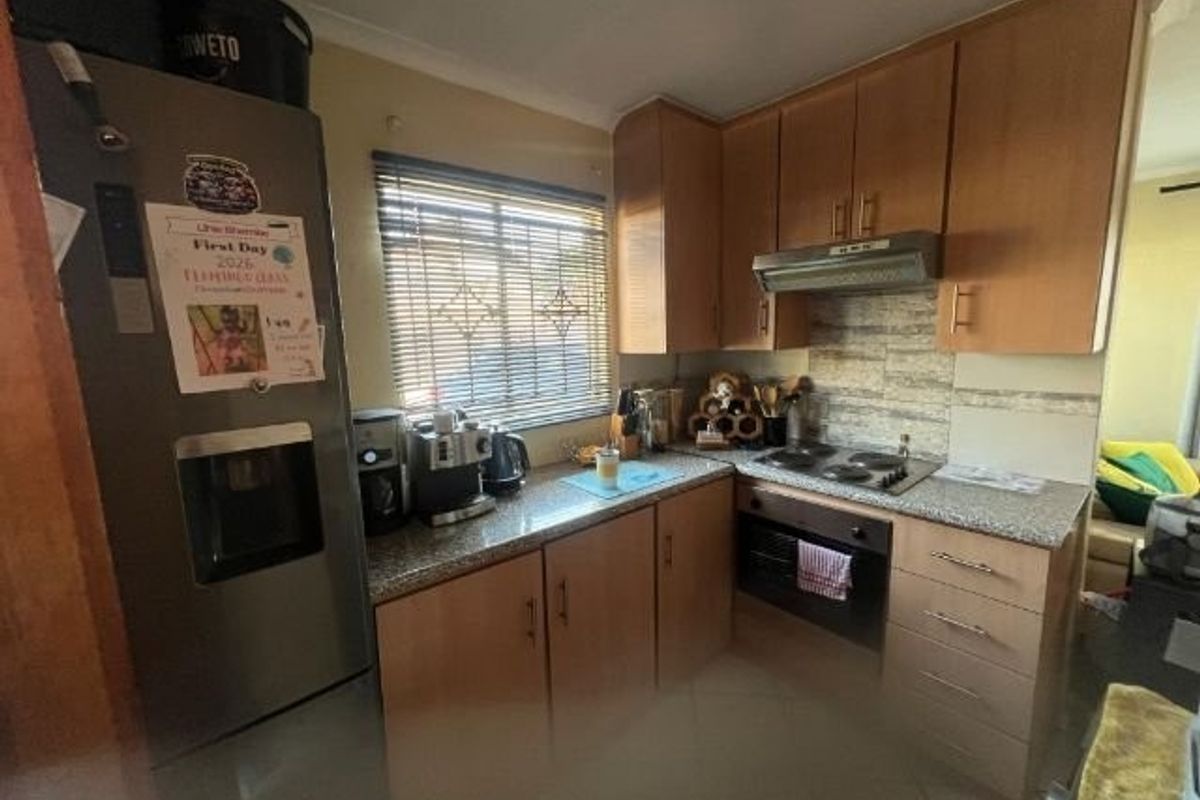 Functional kitchen featuring wood-finish cabinetry, granite countertops, built-in oven, electric hob, and extractor fan with a tiled splashback.