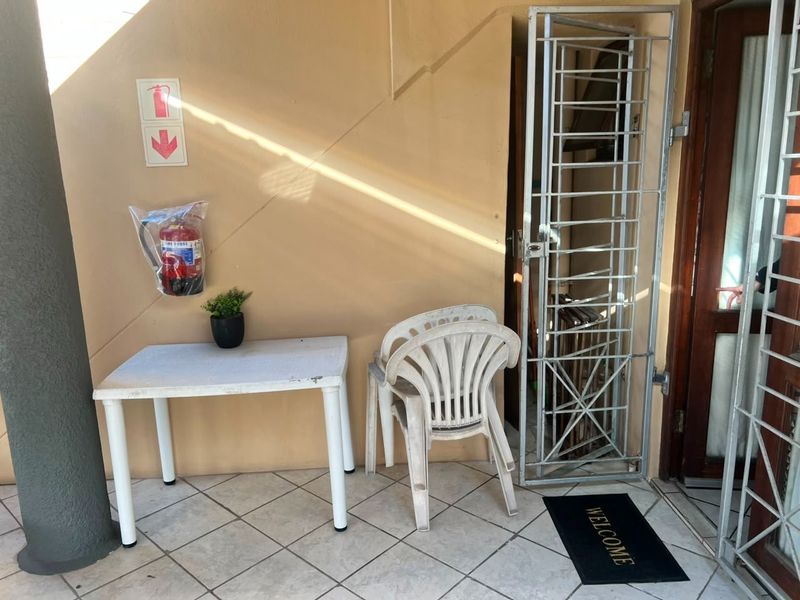 A covered patio area featuring tiled flooring, a security gate, and a wall-mounted fire extinguisher.