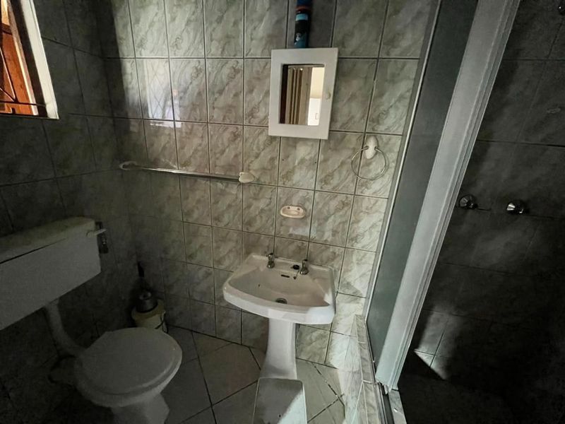 A compact bathroom featuring a pedestal basin, toilet, and shower enclosure with dated ceramic wall and floor tiling.