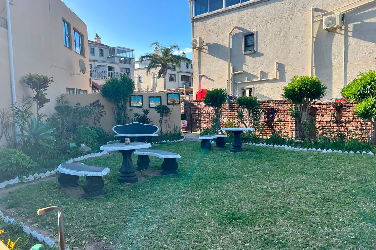 A shared rear garden area featuring a lawn and brick boundary wall, situated between apartment buildings with external air conditioning units.