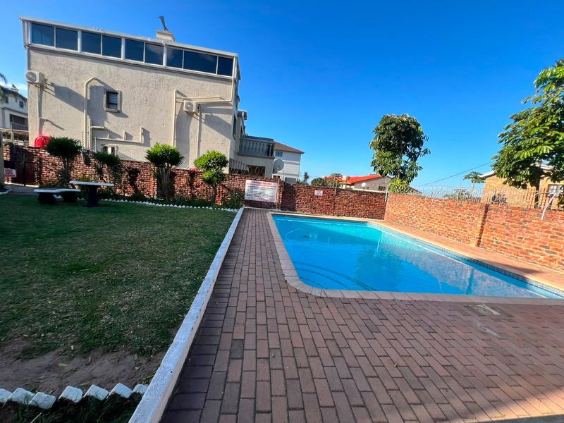Outdoor communal pool area featuring a paved deck, surrounding brick boundary walls, and a well-maintained lawn.