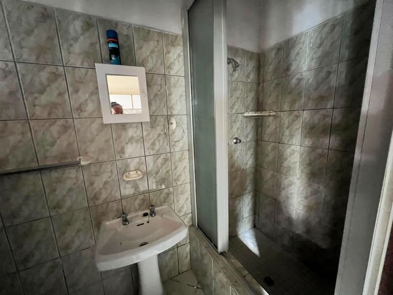 A dated bathroom featuring a pedestal basin and a shower enclosure with full-height wall tiling.