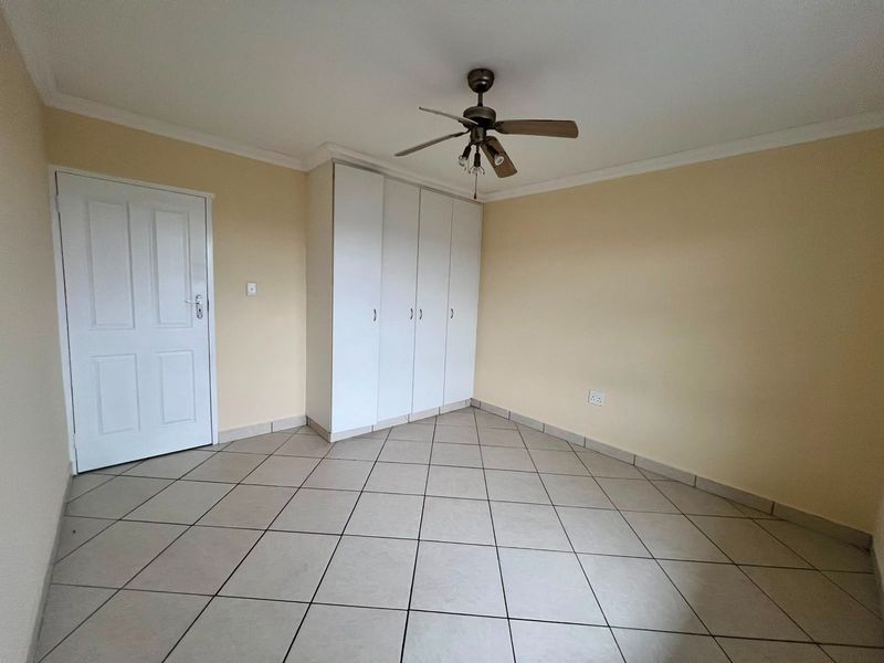 An empty bedroom featuring tiled flooring, built-in cupboards, and a ceiling fan, providing a clean and neutral space ready for personalization.