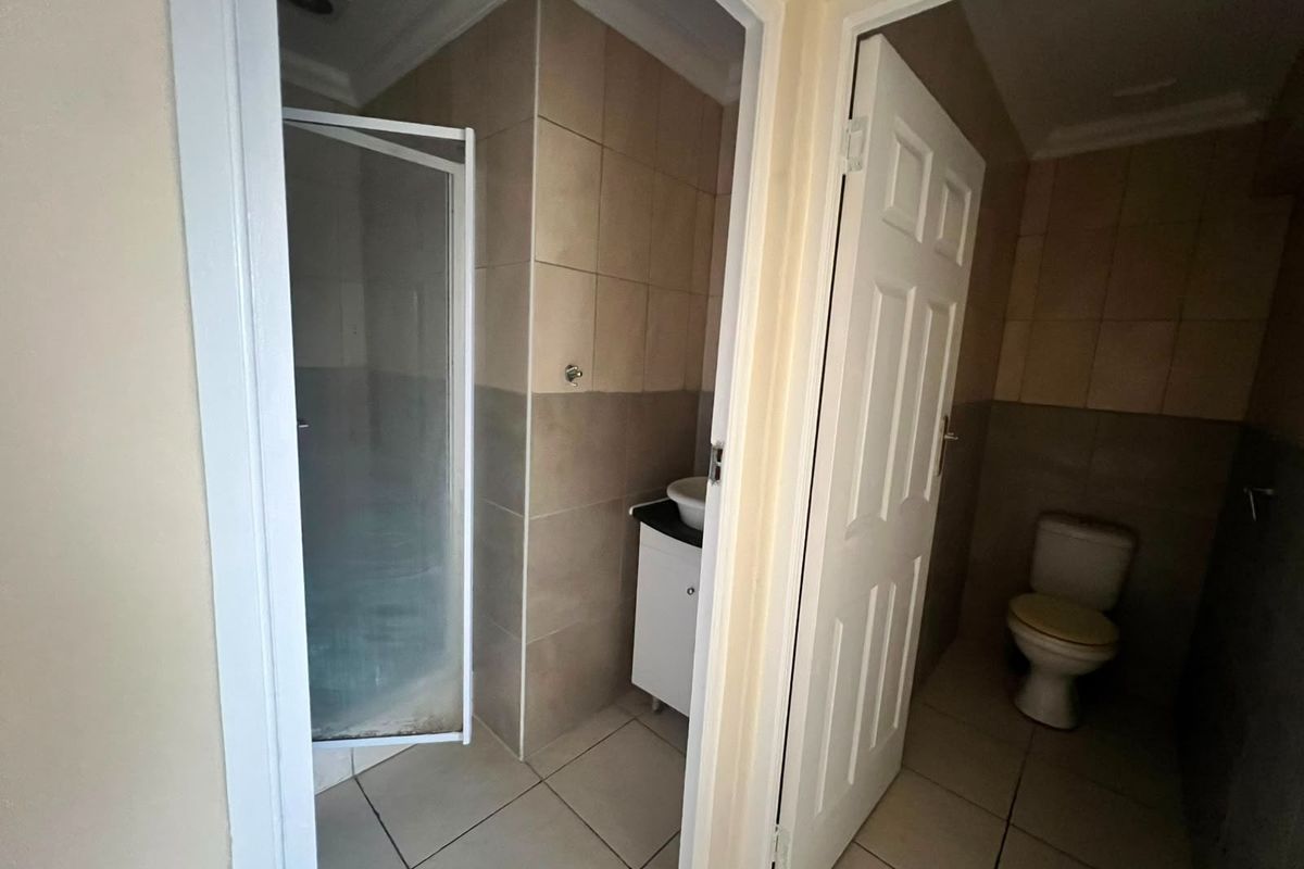 A functional bathroom featuring a separate shower enclosure, vanity basin, and toilet with neutral wall and floor tiling.