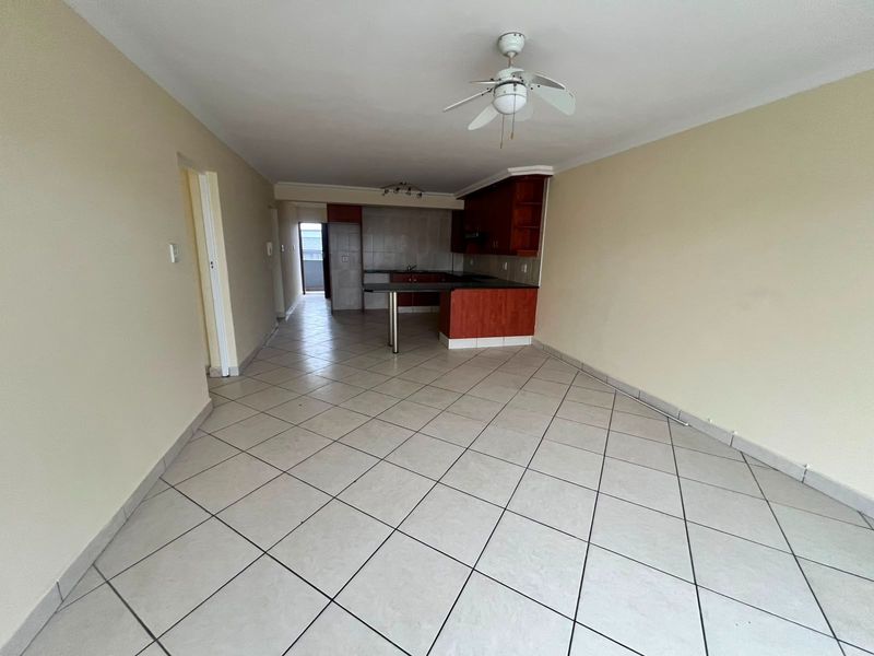 An open-plan living and kitchen area featuring tiled flooring, a breakfast bar, and built-in cabinetry, offering a blank canvas for potential interior design updates.