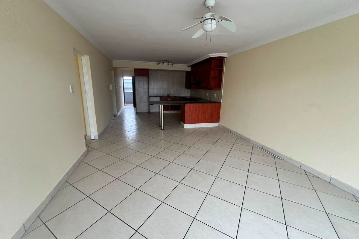 An open-plan living and kitchen area featuring tiled flooring, a breakfast bar, and built-in cabinetry, offering a blank canvas for potential interior design updates.
