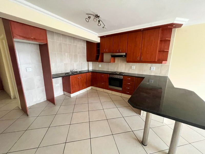 A functional kitchen featuring cherry wood cabinetry, black granite countertops, a breakfast bar, and built-in appliances, finished with neutral floor tiles.