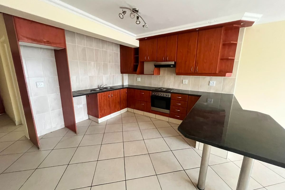 A functional kitchen featuring cherry wood cabinetry, black granite countertops, a breakfast bar, and built-in appliances, finished with neutral floor tiles.