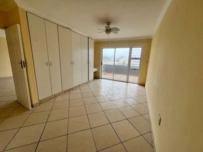 Spacious bedroom featuring built-in cupboards, tiled flooring, a ceiling fan, and direct access to a private balcony through sliding glass doors.