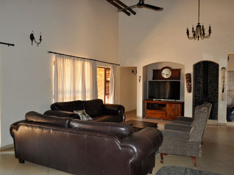Spacious living room featuring a high vaulted ceiling, ceiling fan, tiled flooring, and a distinctive arched alcove with a stone fireplace.