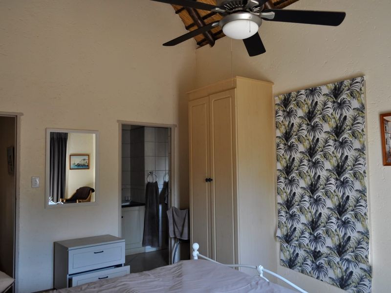 Bedroom featuring a vaulted thatched ceiling, ceiling fan, and built-in wardrobe, with direct access to an en-suite bathroom.