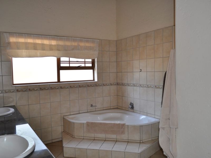 A functional bathroom featuring a corner bathtub, dual vanity sinks, and neutral wall tiling.