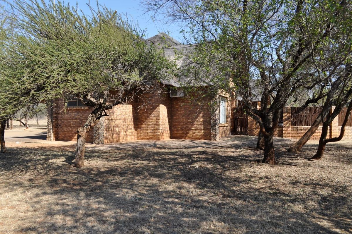 A view of the rear exterior of a face brick house featuring a traditional thatch roof and established trees in the surrounding garden area.