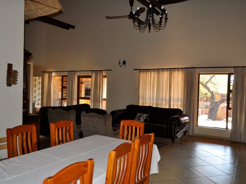 Spacious open-plan living and dining area featuring high ceilings with exposed timber beams, tiled flooring, and large windows providing natural light.