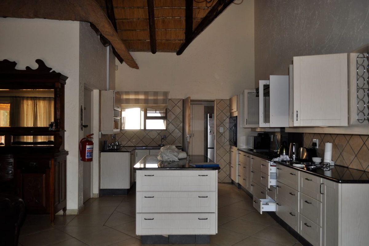 Spacious kitchen featuring a central island, granite countertops, ample built-in cabinetry, and a high-volume ceiling with exposed timber rafters.