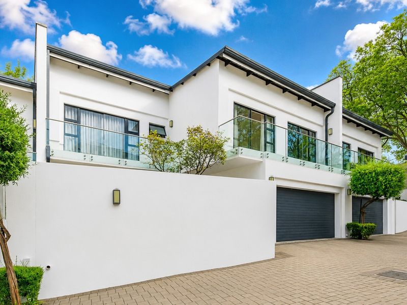 Modern double-storey residential facade featuring a paved driveway, integrated double garages, and upper-level balconies with contemporary glass balustrades.