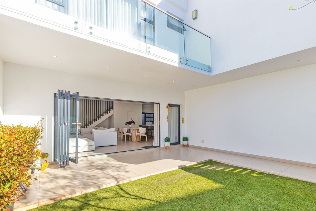 A modern rear courtyard featuring a tiled patio, artificial lawn, and seamless indoor-outdoor flow through large bi-fold doors to the open-plan living area.