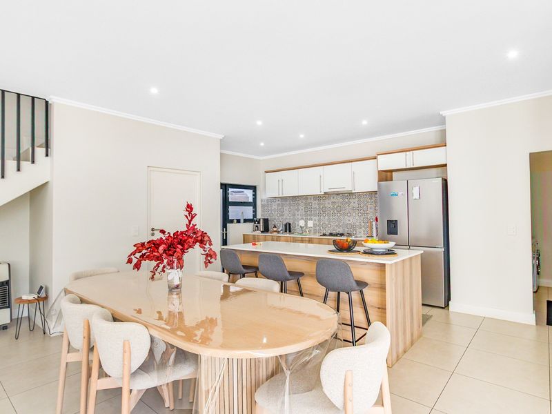 Modern open-plan kitchen and dining area featuring a central island, contemporary cabinetry, patterned backsplash, and a staircase with a sleek metal railing.