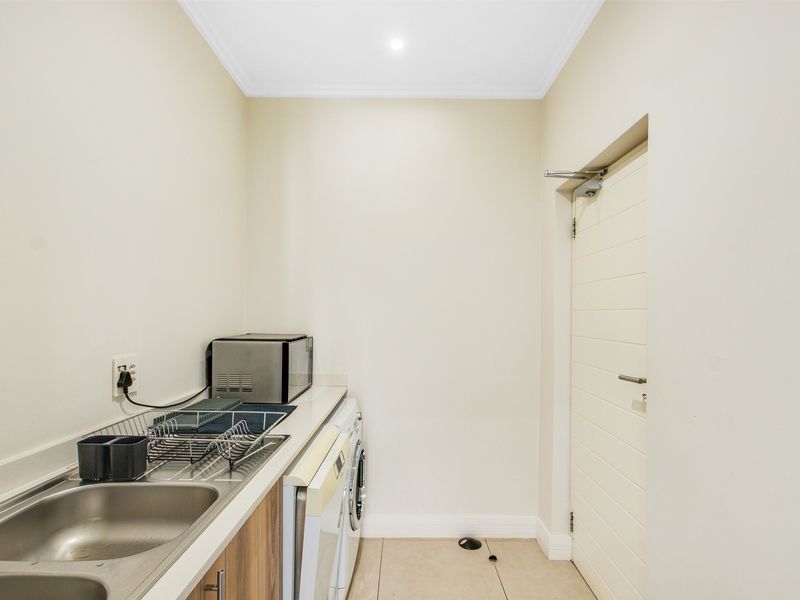 A functional laundry room featuring a stainless steel sink, built-in cabinetry, and tiled flooring with direct access to an internal door.