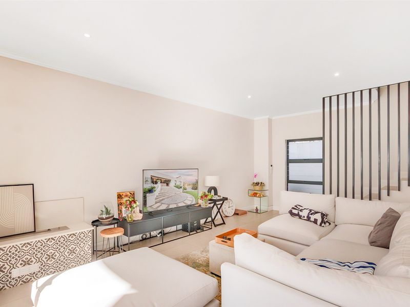 A bright and modern living room featuring tiled flooring, recessed downlighting, and a contemporary metal staircase balustrade.