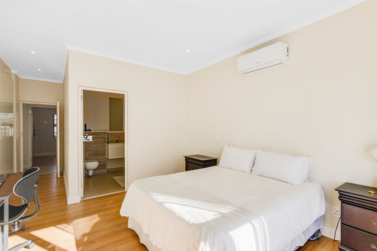 A well-maintained bedroom featuring laminate flooring, recessed lighting, a wall-mounted air conditioning unit, and direct access to an en-suite bathroom.