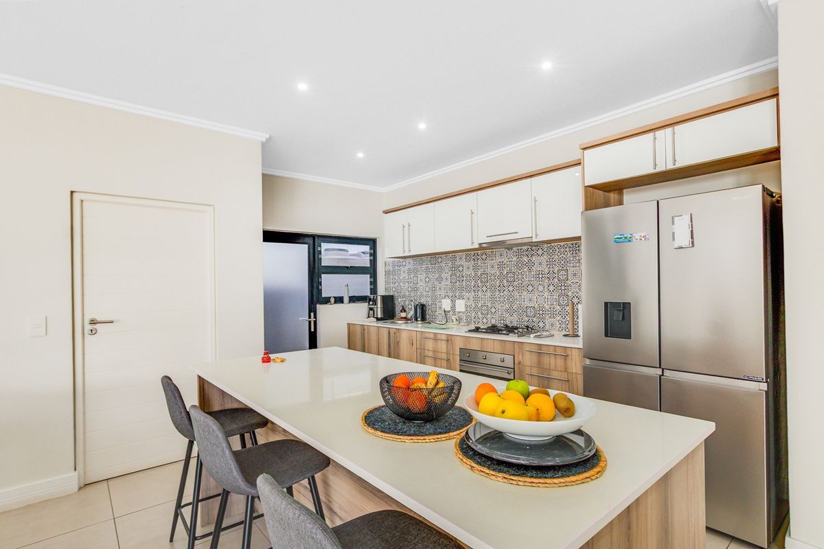 Modern kitchen featuring a central island with stone countertops, built-in cabinetry, gas hob, oven, and stylish patterned tile backsplash.