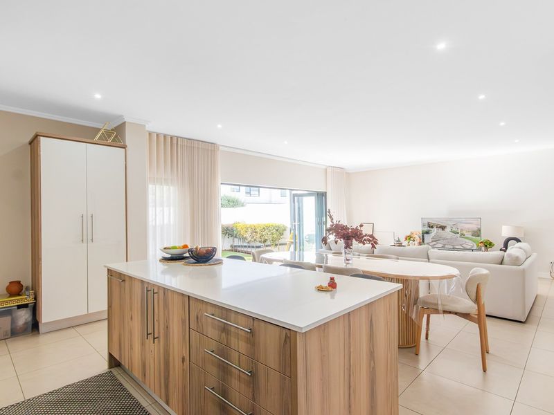 Spacious open-plan living area featuring a modern kitchen island with stone countertops, tiled flooring, and seamless access to the outdoor patio through sliding glass doors.