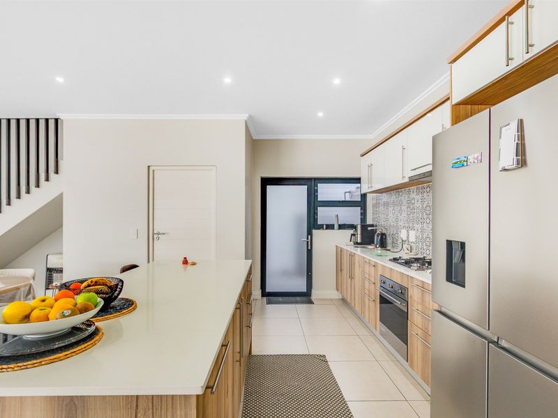 Modern kitchen featuring a central island, sleek laminate cabinetry, built-in oven, gas hob, and stylish patterned tile backsplash with neutral floor tiles.