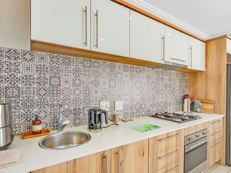 Modern kitchen featuring wood-grain cabinetry, white stone countertops, a gas hob with extractor fan, and a decorative patterned tile backsplash.