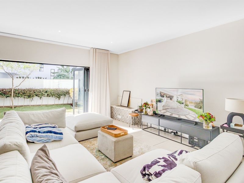 Bright living room featuring large aluminium stacker doors that open onto a private garden, complemented by neutral tiled flooring and recessed lighting.