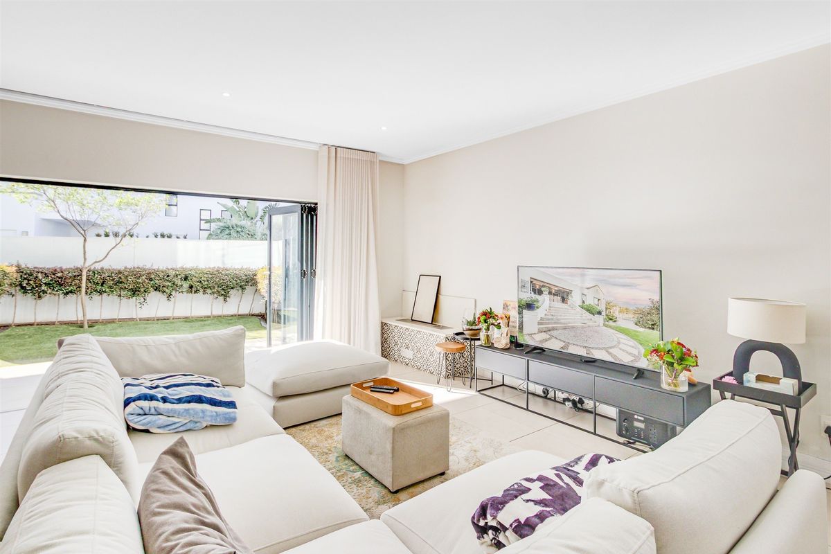 Bright living room featuring large aluminium stacker doors that open onto a private garden, complemented by neutral tiled flooring and recessed lighting.