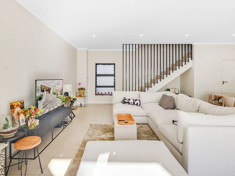 A bright and modern living room featuring tiled flooring, recessed downlights, and a contemporary staircase with a sleek metal balustrade.