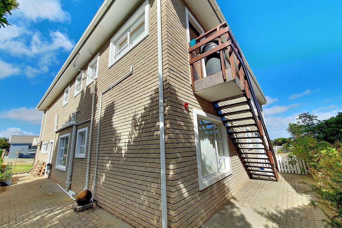 Exterior view of the side of the house featuring a brick facade, paved ground area, and an external timber staircase leading to an upper balcony.