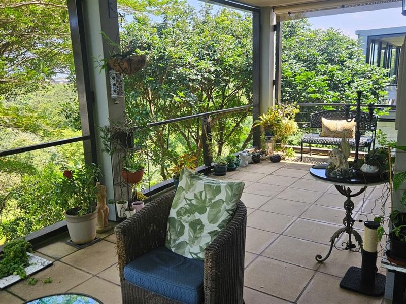A covered balcony featuring tiled flooring, a metal safety railing, and a retractable awning, offering an elevated view of the surrounding greenery.